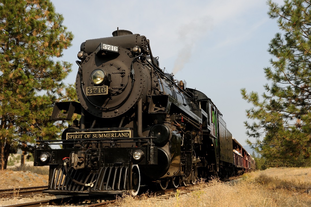 A steam train coming off of a trestle with people waving